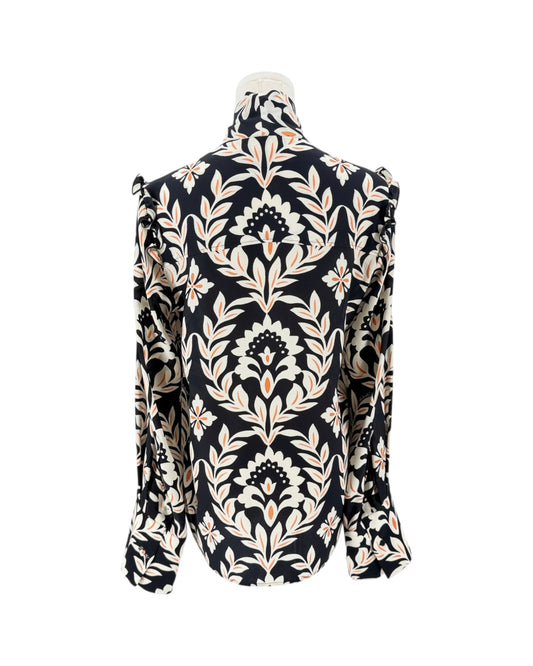 A long-sleeve high-neck blouse with a dramatic ruffled collar and shoulders, featuring an intricate black, beige, and white damask floral pattern, displayed on a mannequin against a white background.