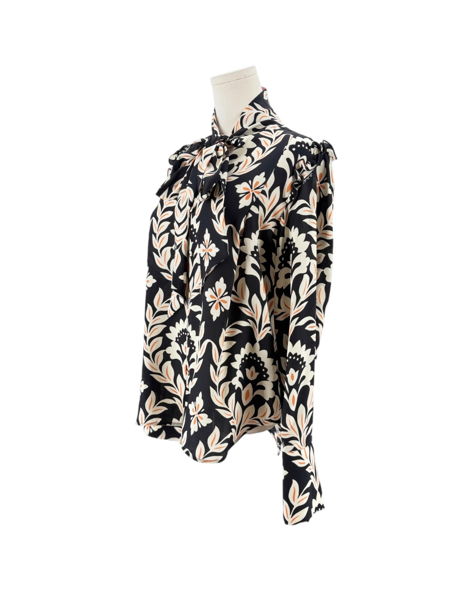 A long-sleeve blouse with a black background and a beige floral pattern, displayed on a mannequin torso against a white background.
