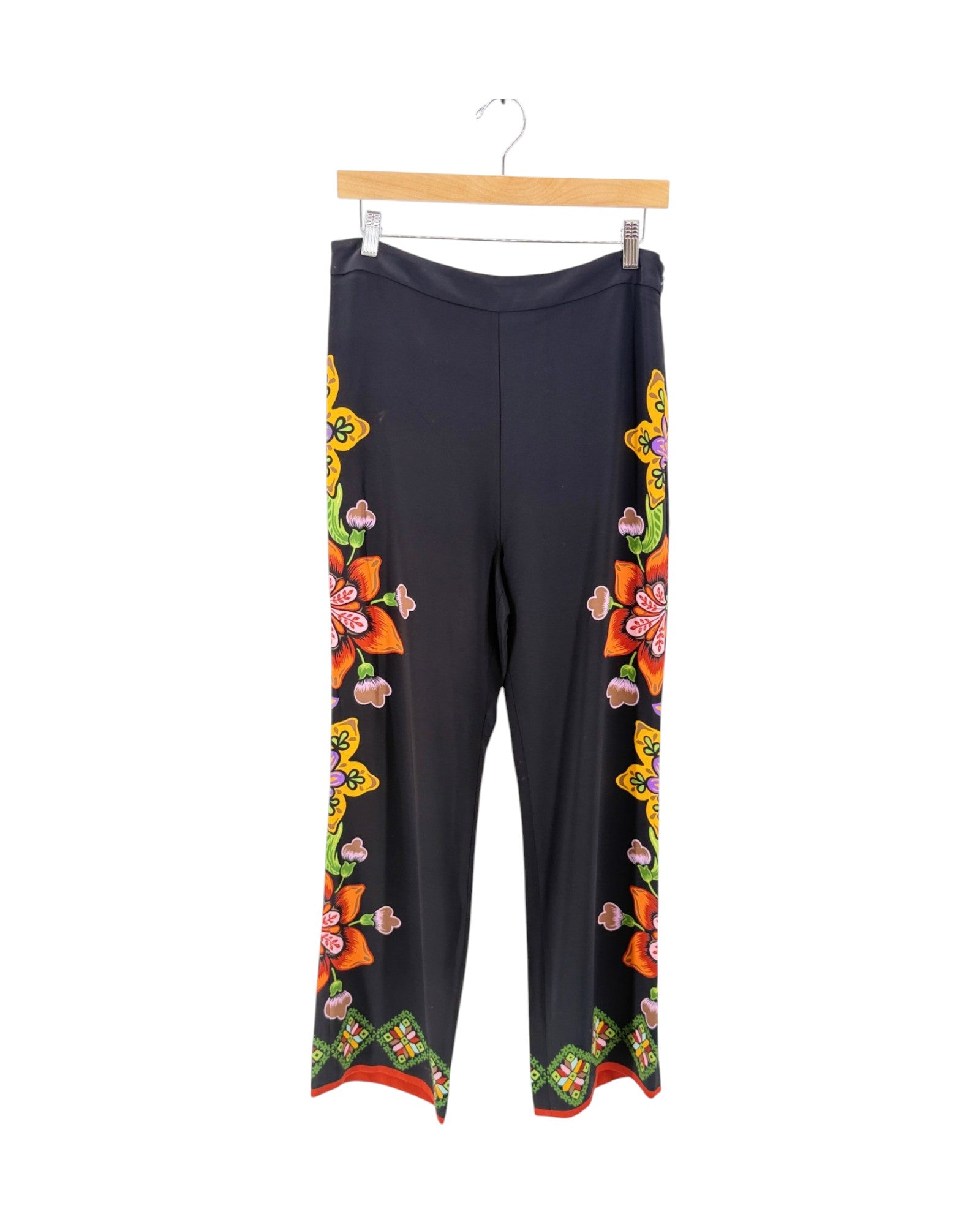 Black wide-leg pants with colorful floral and butterfly patterns down the sides, hanging from a wooden hanger against a white background.