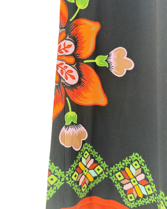 A close-up of a dark charcoal gray fabric featuring a vibrant orange floral print and a green geometric pattern along the hem.