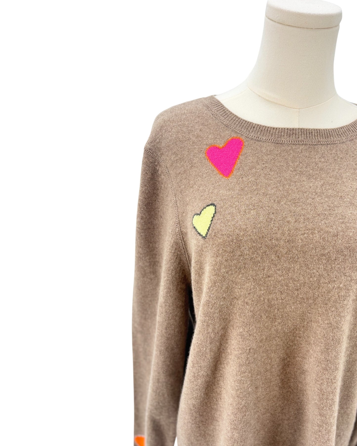 Tan sweater with colorful heart patterns on a mannequin against a white background