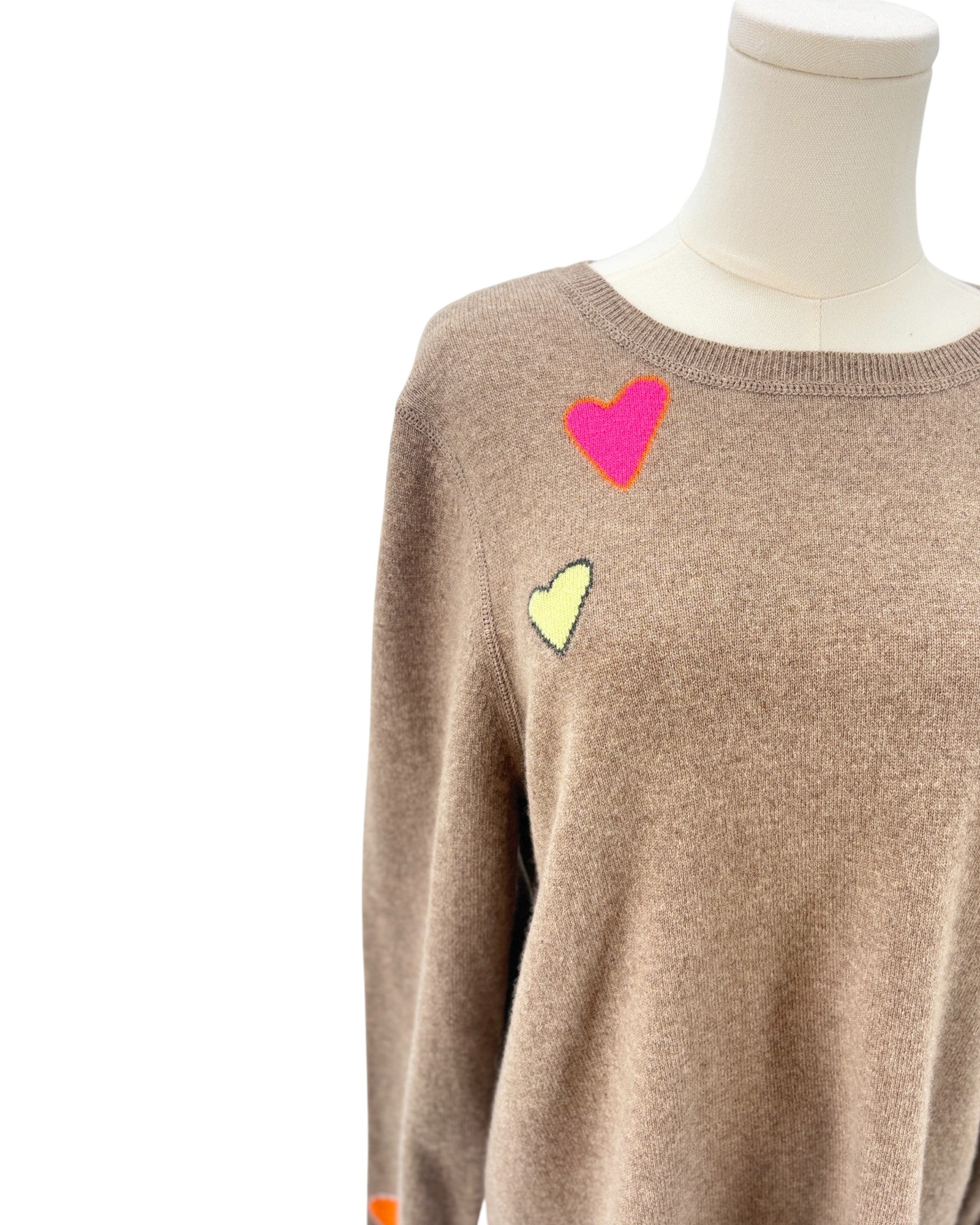 Tan sweater with colorful heart patterns on a mannequin against a white background