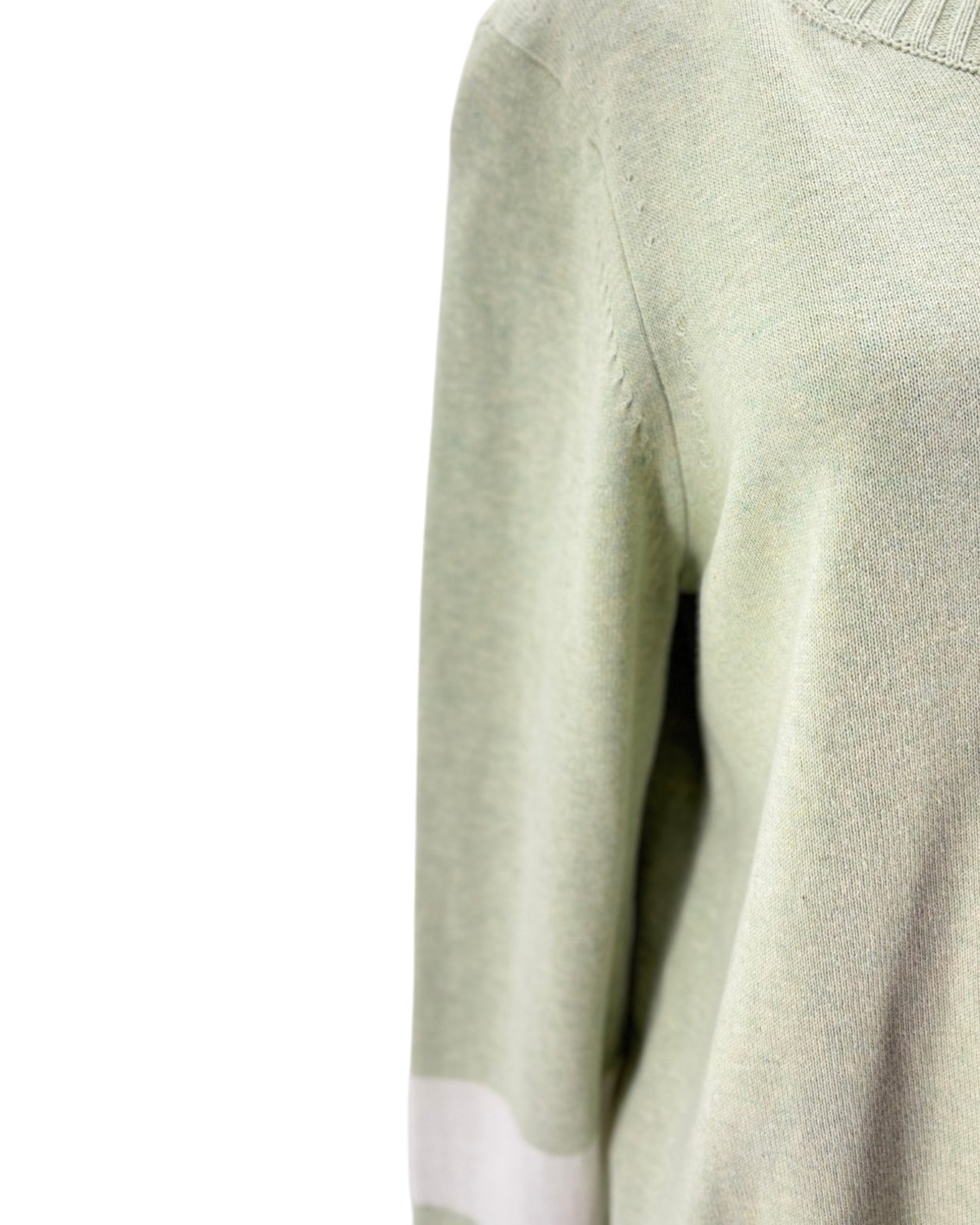 Close-up of a light green sweater with a white patch on a white background