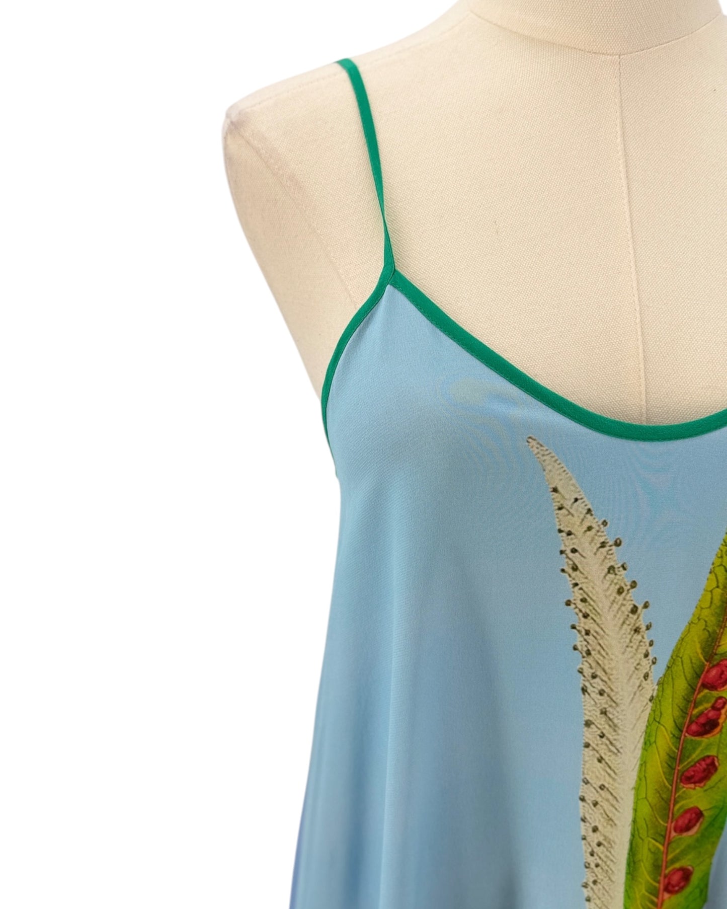 Light blue sleeveless dress with green trim and leaf design on a mannequin against a white background