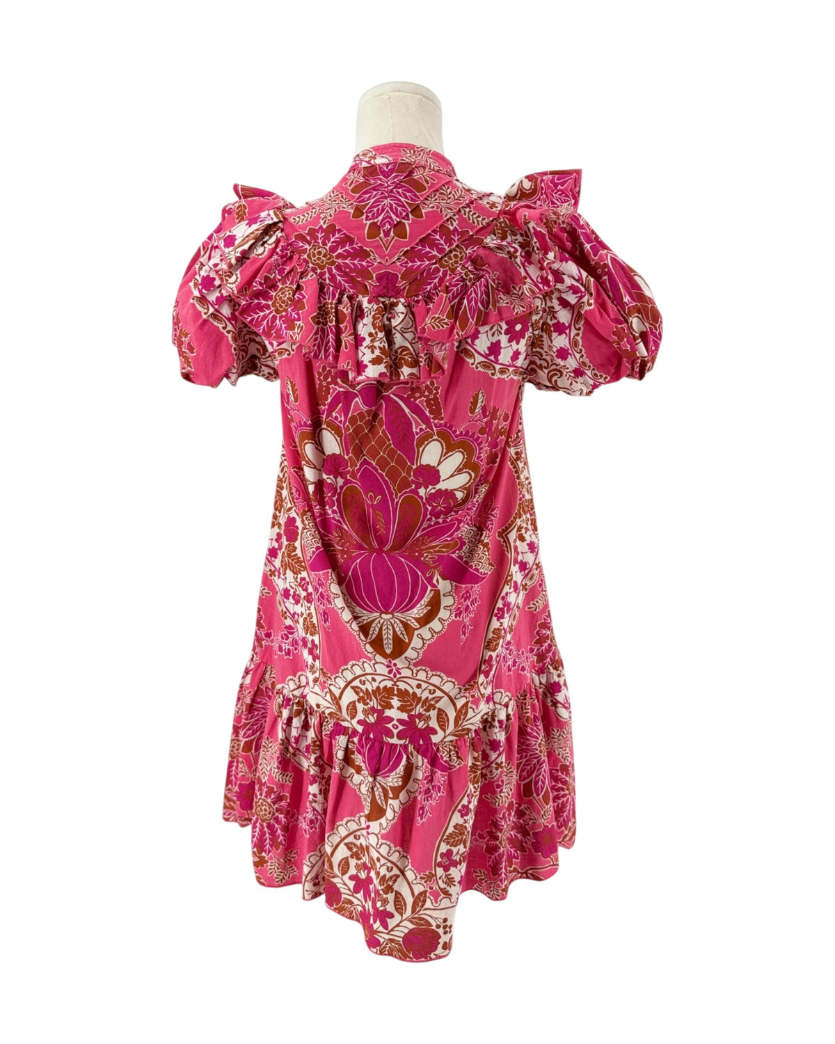 A pink patterned dress displayed on a mannequin torso against a plain white background. The dress features puff sleeves, a ruffled yoke, and a tiered ruffle hem, decorated with a vibrant floral and paisley print in pink, brown, and white.