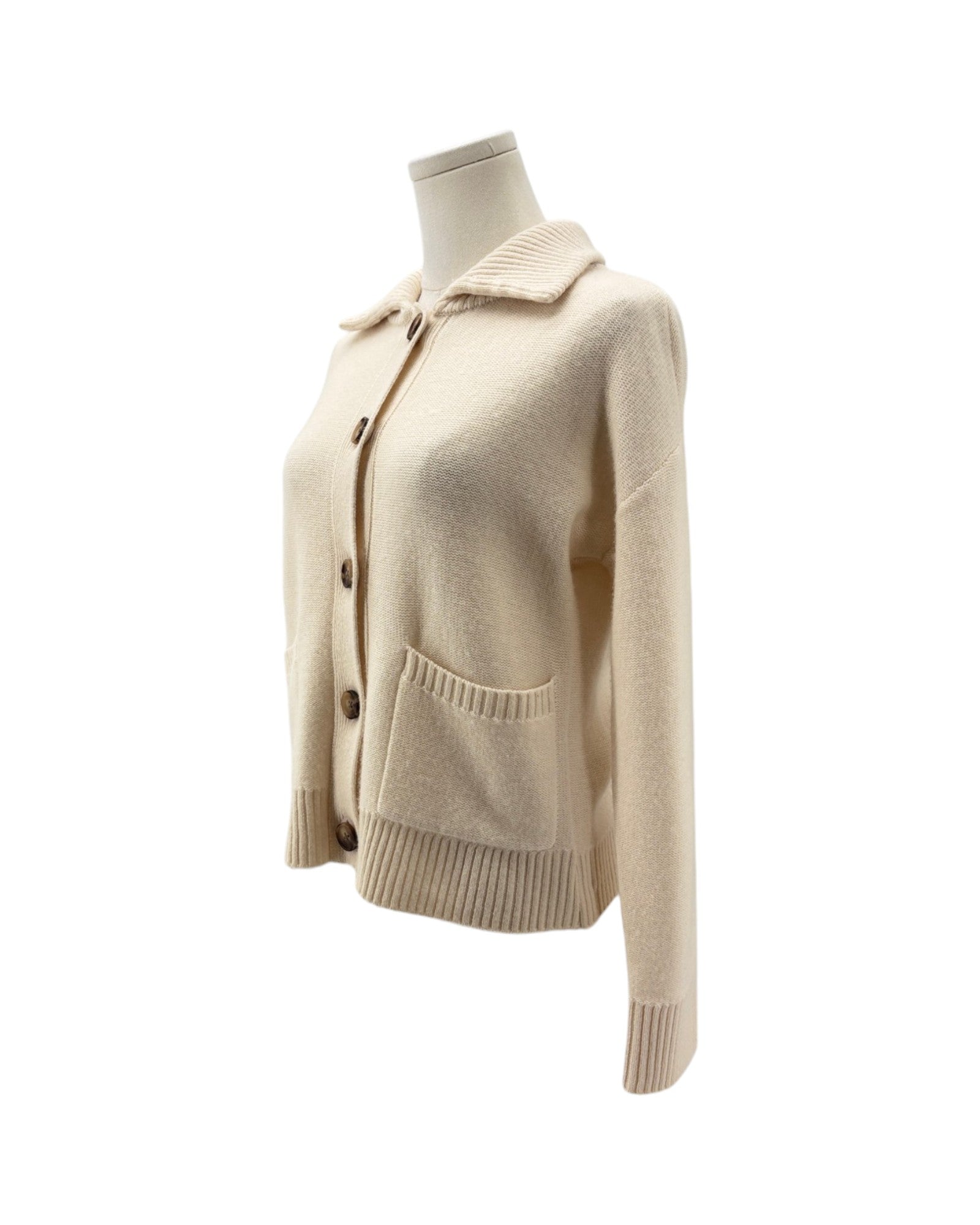 A cream-colored knit cardigan sweater with a pointed collar, button-front closure, and front patch pocket, displayed on a mannequin torso against a plain white background.