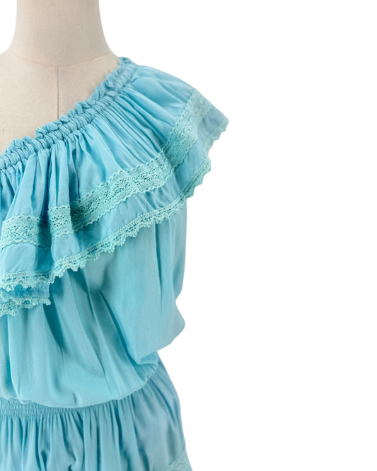 A light blue ruffled top with lace trim displayed on a mannequin against a white background.