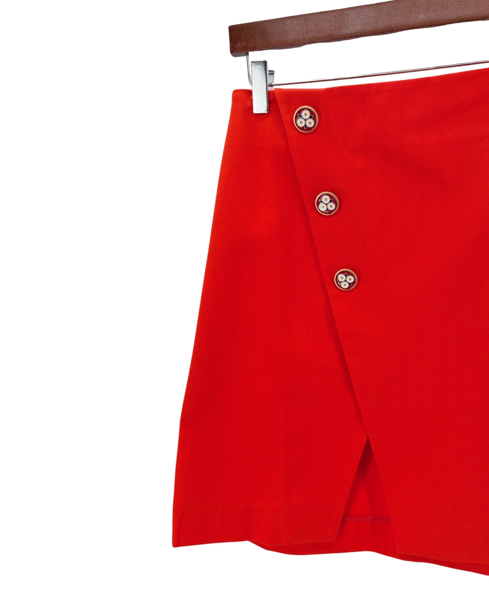 Red skirt with button details on a hanger against a white background