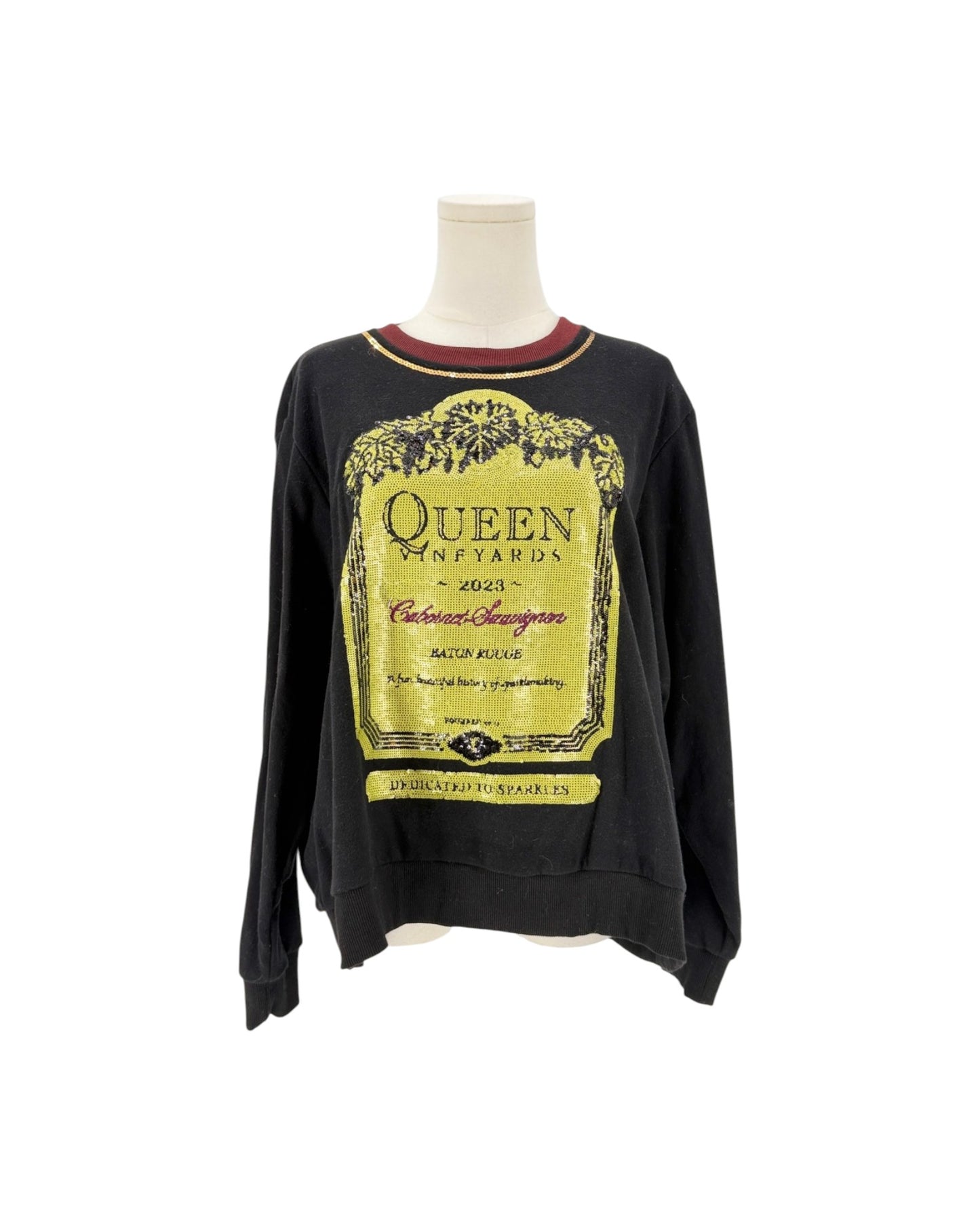 A black long-sleeve crewneck sweatshirt displayed on a mannequin torso against a white background. The sweatshirt features a large yellow vintage wine label graphic on the front with 'Queen Vineyards' text, and a small red inner collar.