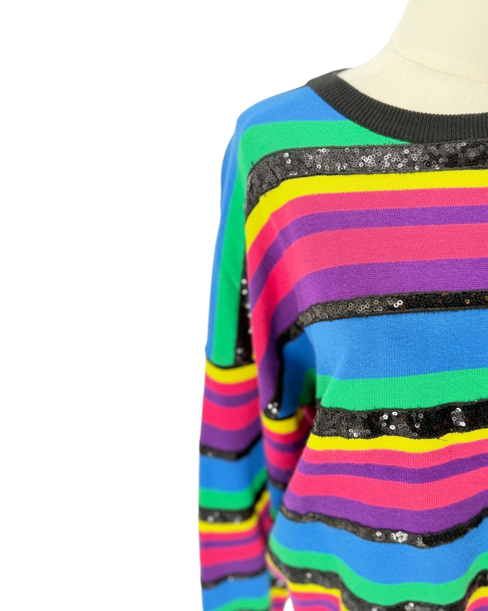 A close-up of a colorful striped knit sweater on a mannequin torso, featuring horizontal bands of blue, green, yellow, pink, purple, and black with sequined trim.