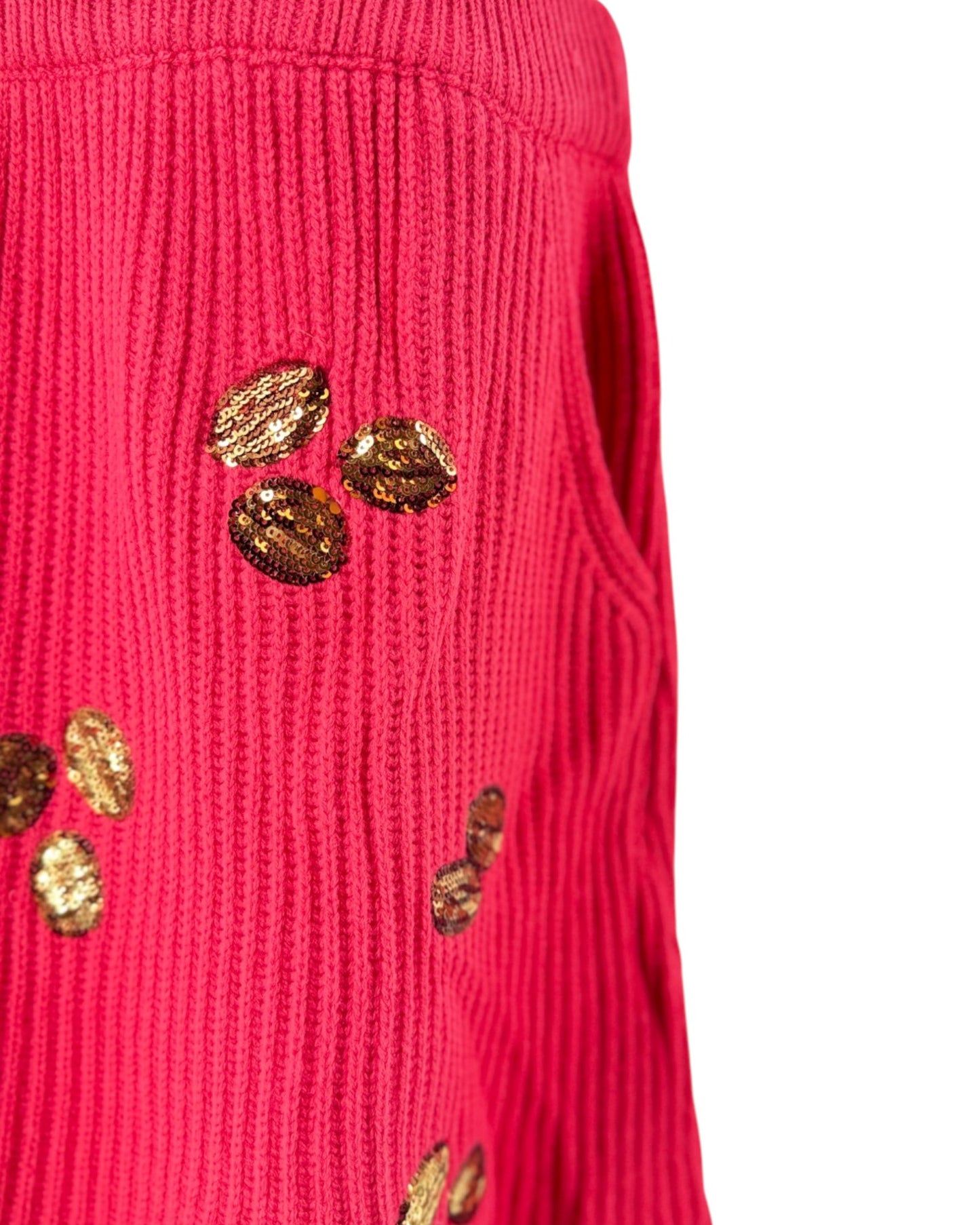 A close-up of a bright pink ribbed knit sweater featuring decorative metallic gold sequins arranged on the front, set against a plain white background.