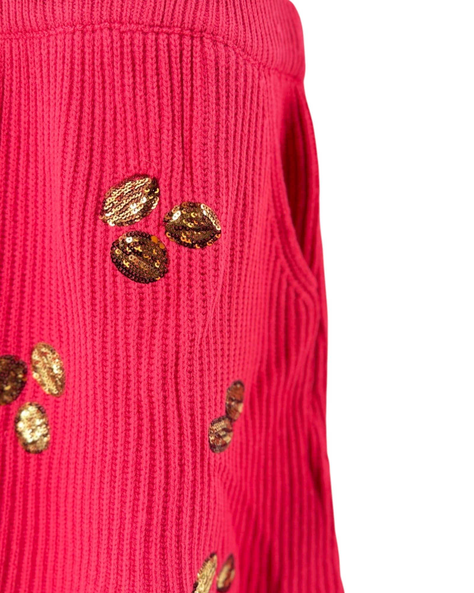 A close-up of a bright pink ribbed knit sweater featuring decorative metallic gold sequins arranged on the front, set against a plain white background.