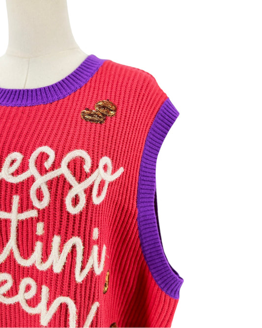 A close-up of a sleeveless ribbed knit sweater vest on a mannequin, featuring a bright pink body with purple ribbed trim, white script lettering, and a small gold heart embellishment.