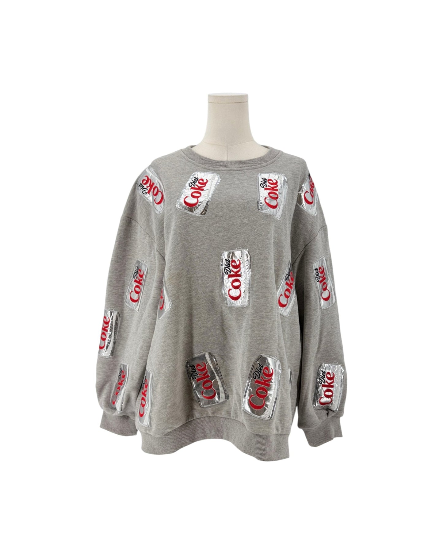 A gray crewneck sweatshirt displayed on a mannequin torso, featuring an all-over print of silver Coca-Cola cans with red script logos.