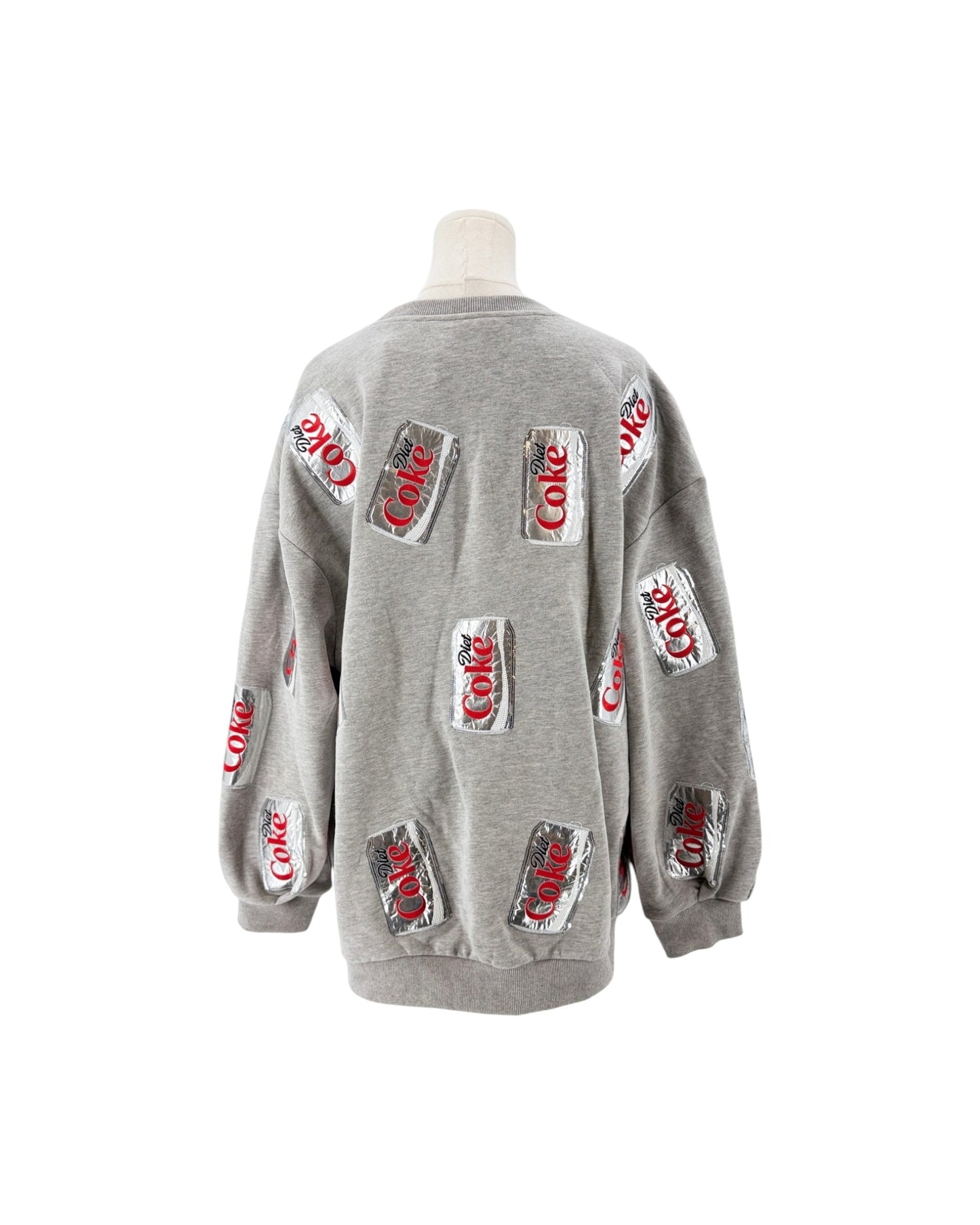 A light gray crewneck sweatshirt displayed on a mannequin torso, featuring multiple printed Coca-Cola can graphics on the front and sleeves.