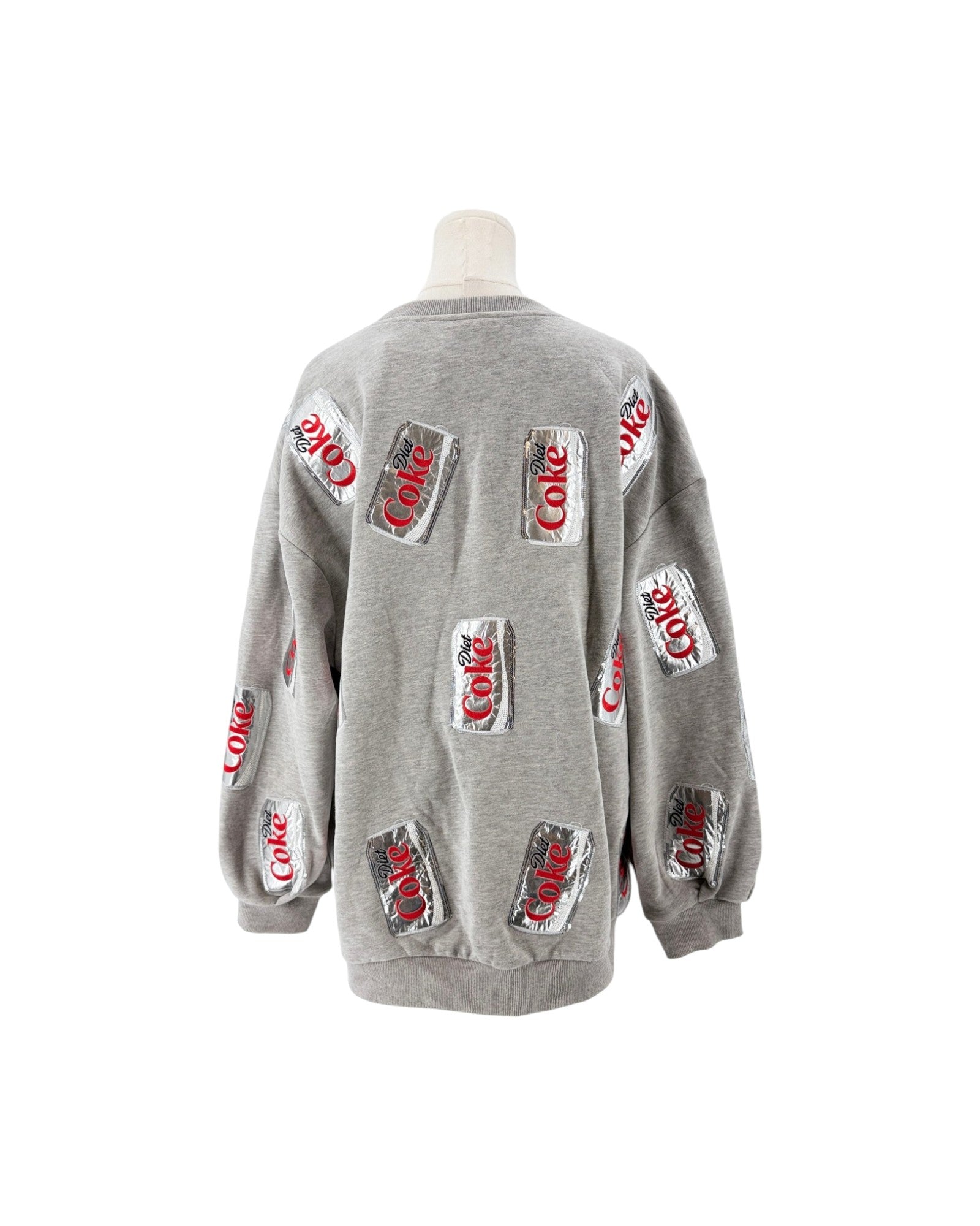 A light gray crewneck sweatshirt displayed on a mannequin torso, featuring multiple printed Coca-Cola can graphics on the front and sleeves.