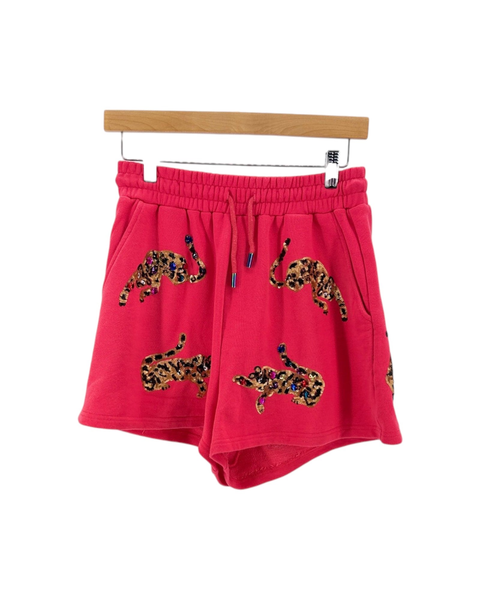 Bright pink drawstring shorts with leopard-print motifs, hanging on a wooden hanger against a white background.