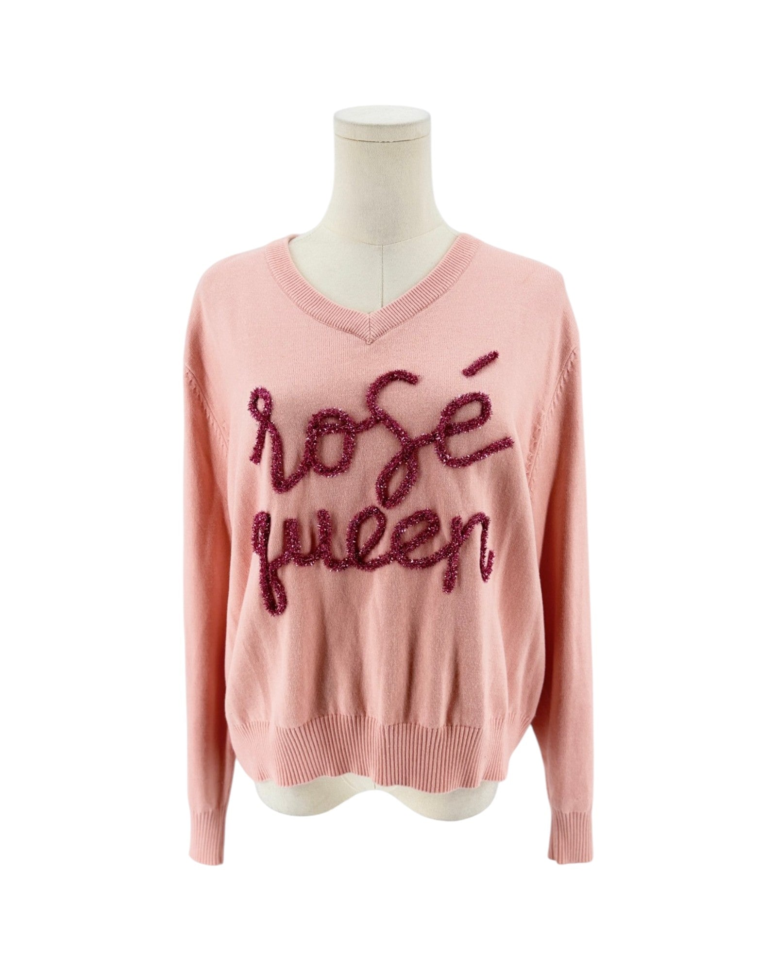 A light pink knit sweater with a V-neck and long sleeves, featuring the words 'rosé queen' written across the chest in dark pink sequined script, displayed on a mannequin torso against a white background.