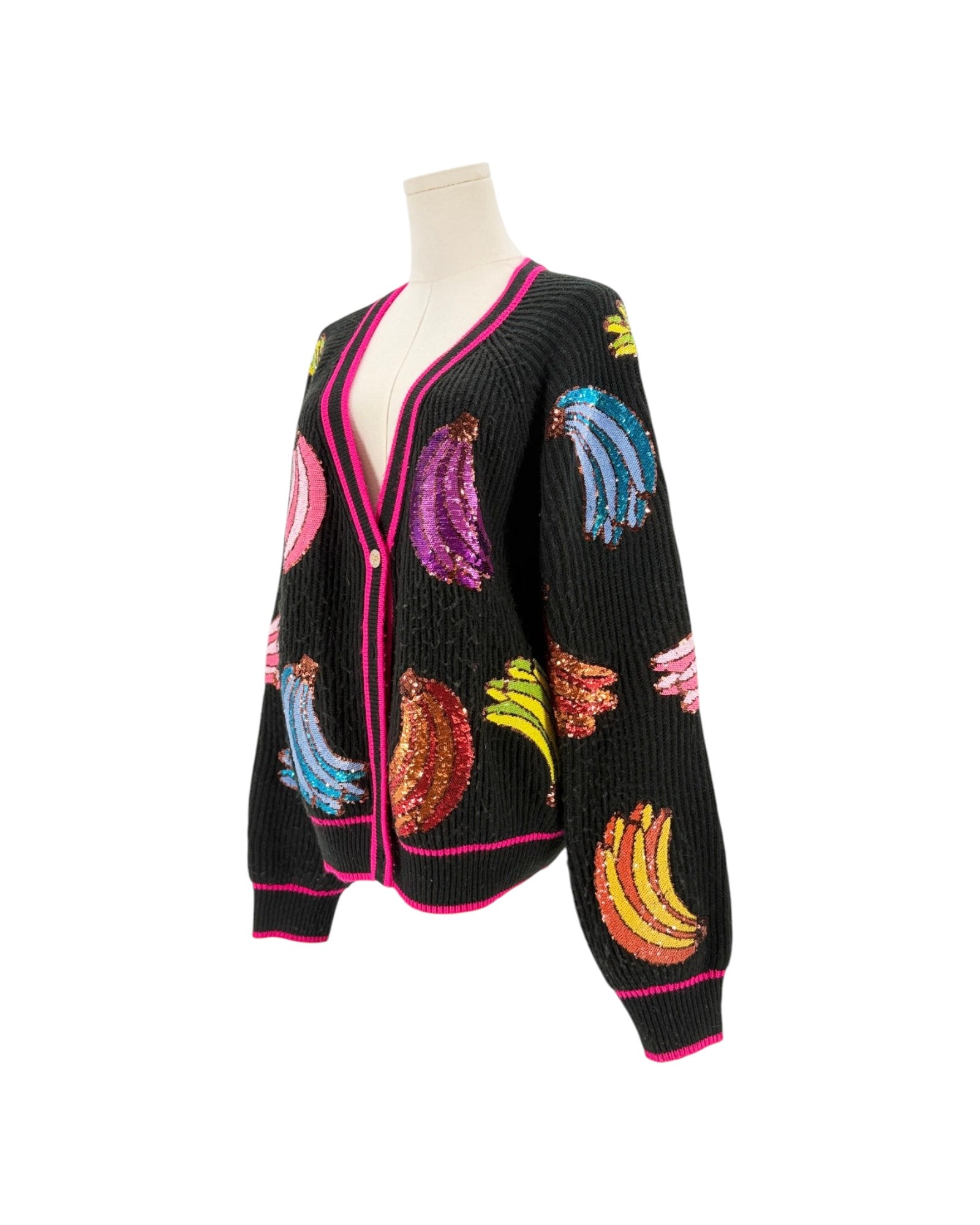 A black ribbed knit cardigan sweater displayed on a mannequin torso against a white background. The cardigan features vibrant, multicolored sequined banana motifs and hot pink trim along the edges.