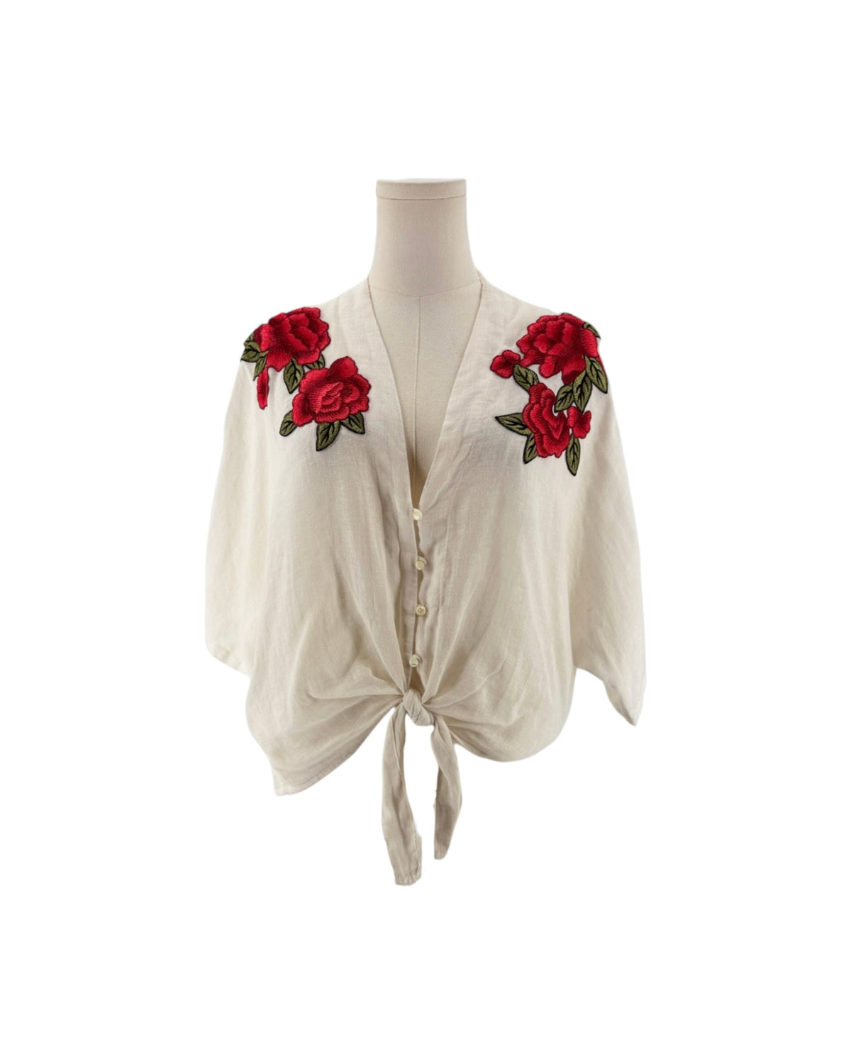 White 3/4 sleeve top with red and green embroidered flowers with a button front and bottom tie. on a mannequin on a white background