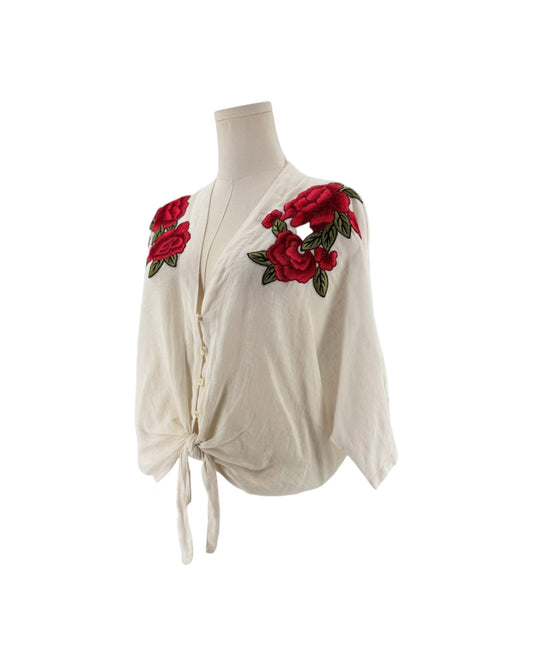 White 3/4 sleeve top with red and green embroidered flowers with a button front and bottom tie. on a mannequin on a white background