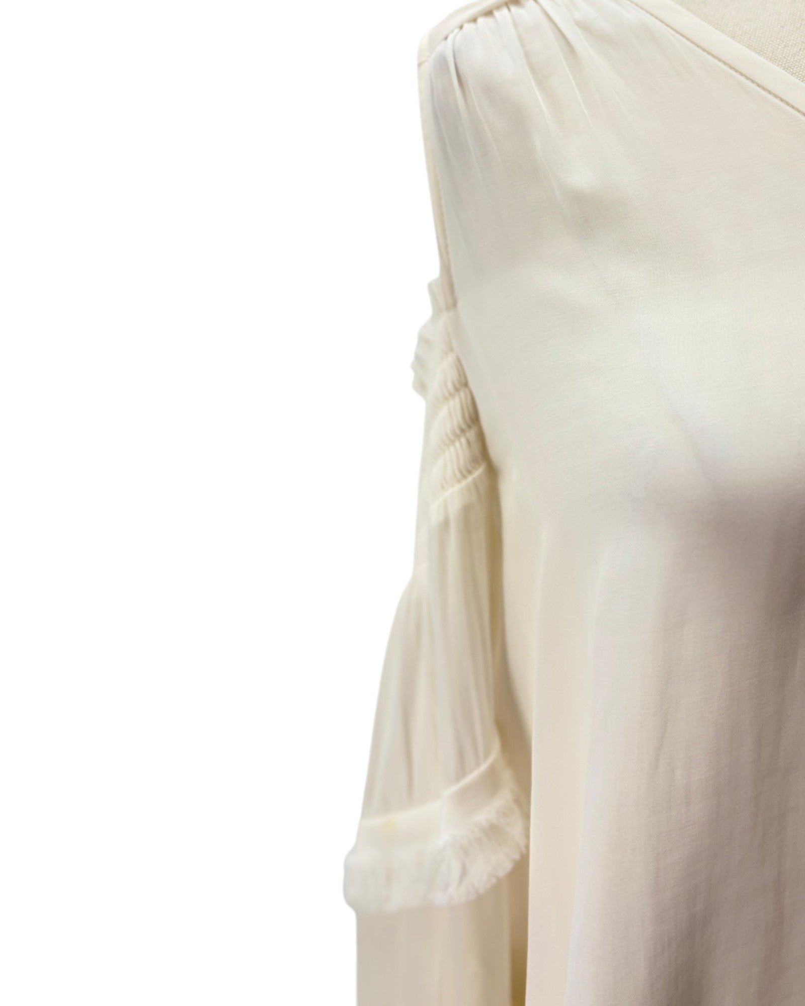 Close-up of a cream-colored off-the-shoulder blouse with gathered sleeves and a smocked bodice, shown on a mannequin against a white background.