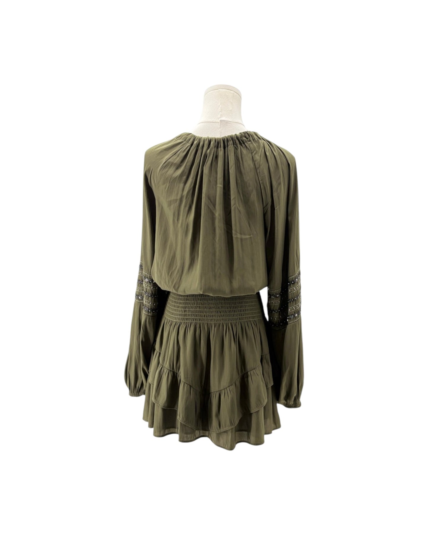 An olive green long-sleeve dress displayed on a white mannequin torso against a plain white background. The dress features a gathered, pleated bodice, a smocked elastic waistband, and tiered ruffles on the skirt, with dark patterned embroidery on the sleeves.