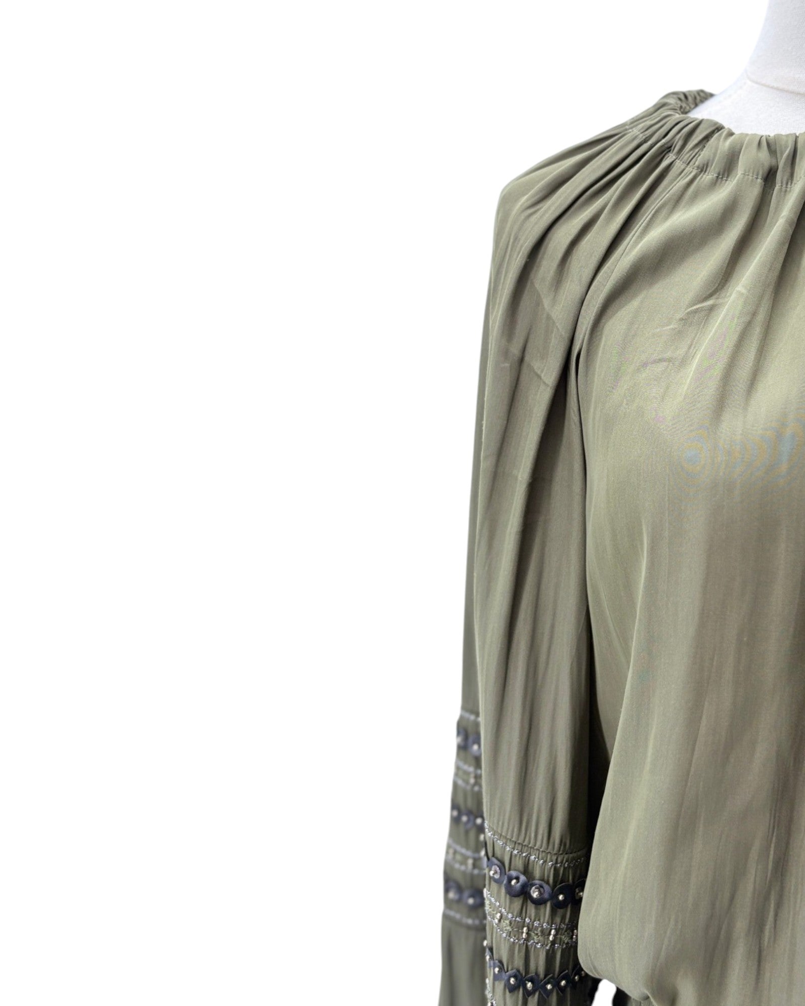 An olive green long-sleeve dress with a gathered, pleated neckline and decorative embroidered trim with small blue beads on the cuffs, shown on a mannequin against a white background.