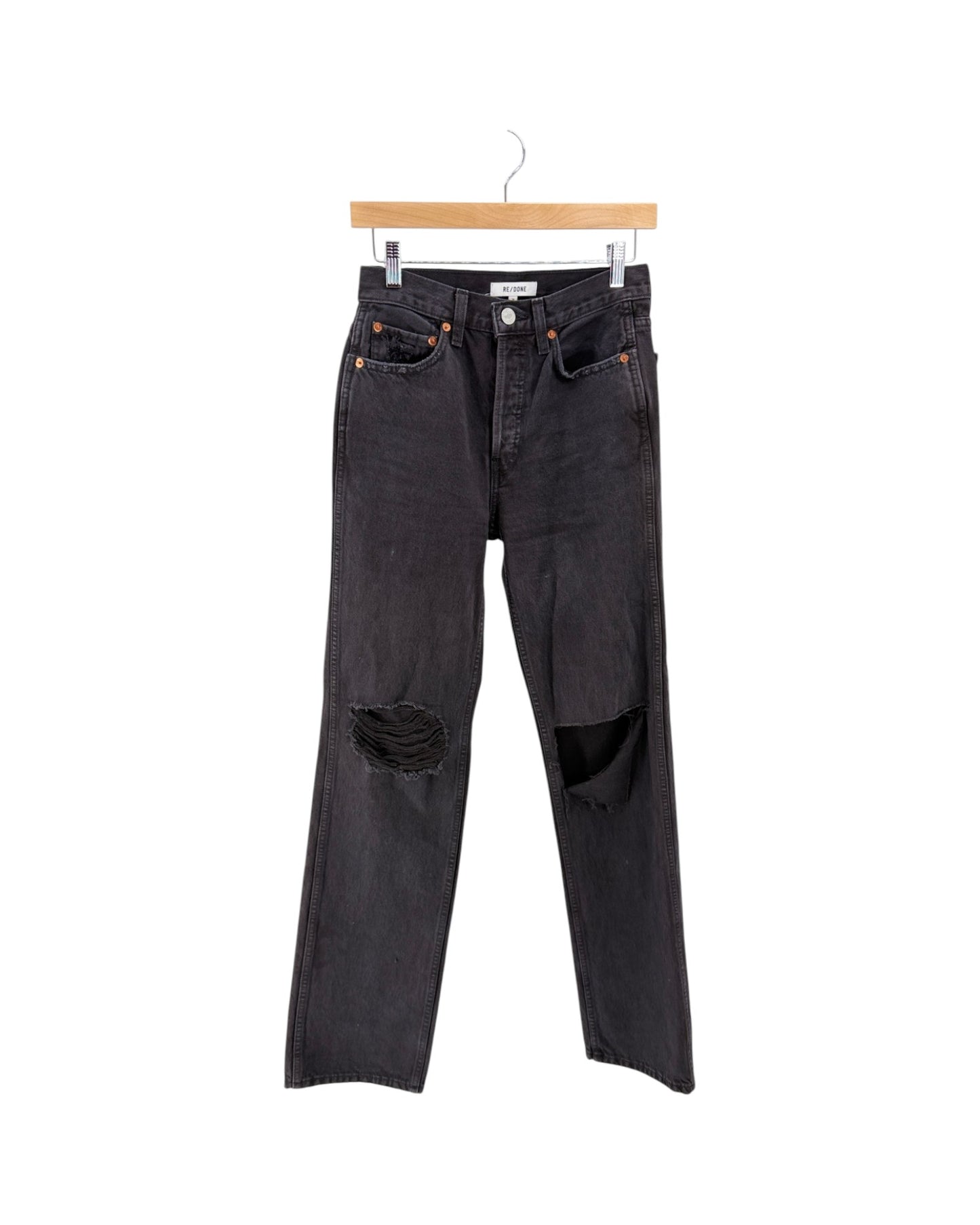 Black distressed denim jeans with ripped knees, hanging from a wooden hanger against a plain white background.
