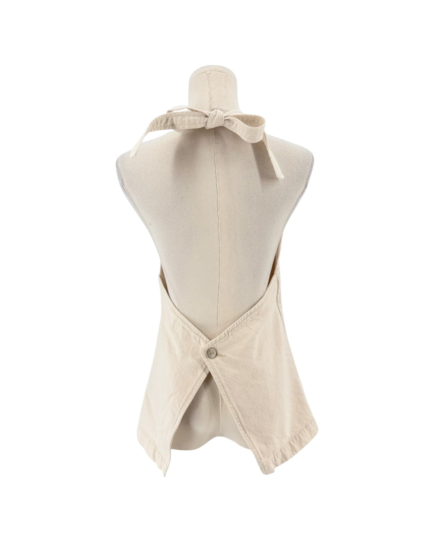 A cream-colored linen apron with a tie-neck design and a buttoned back closure, displayed on a mannequin torso against a white background.