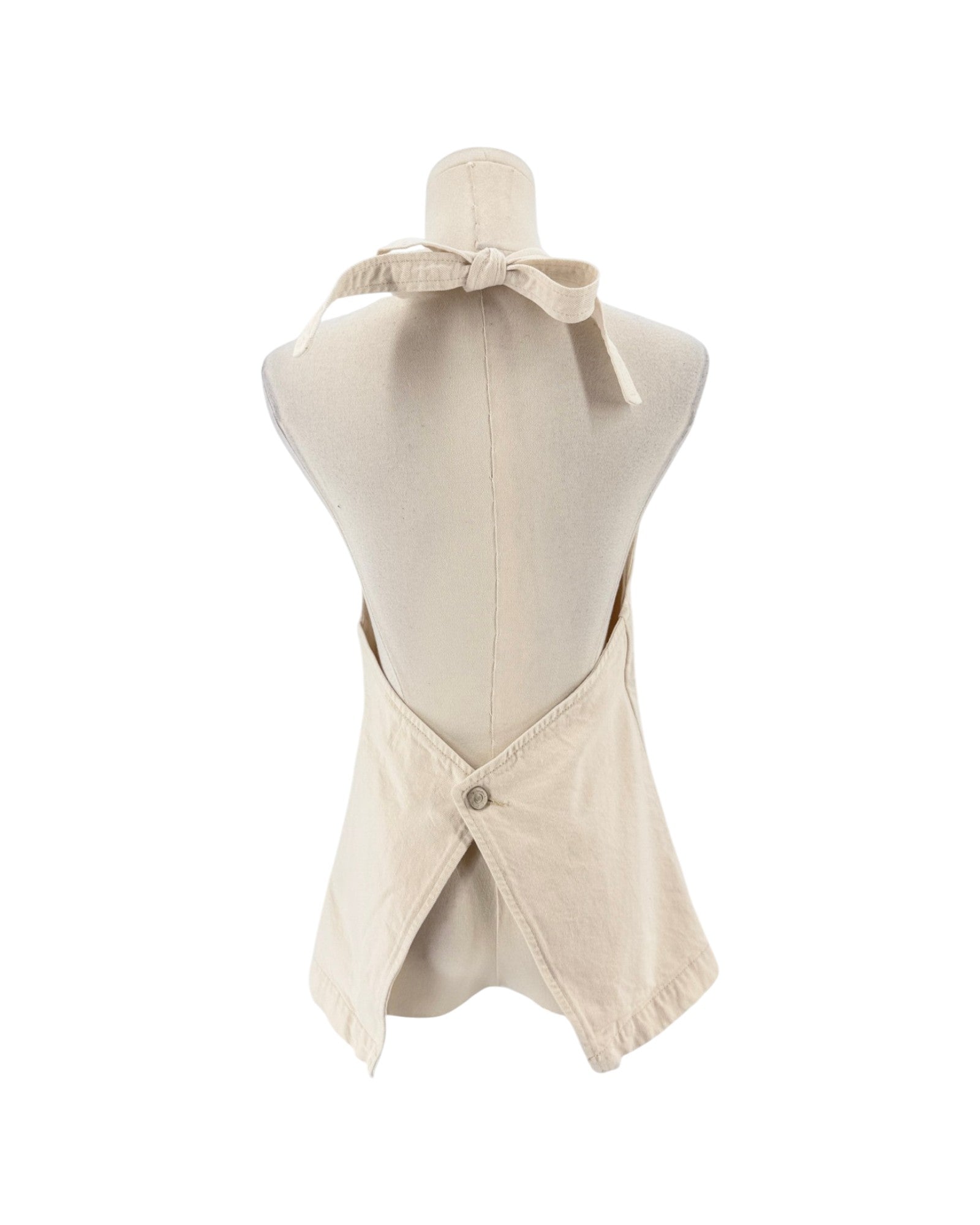 A cream-colored linen apron with a tie-neck design and a buttoned back closure, displayed on a mannequin torso against a white background.