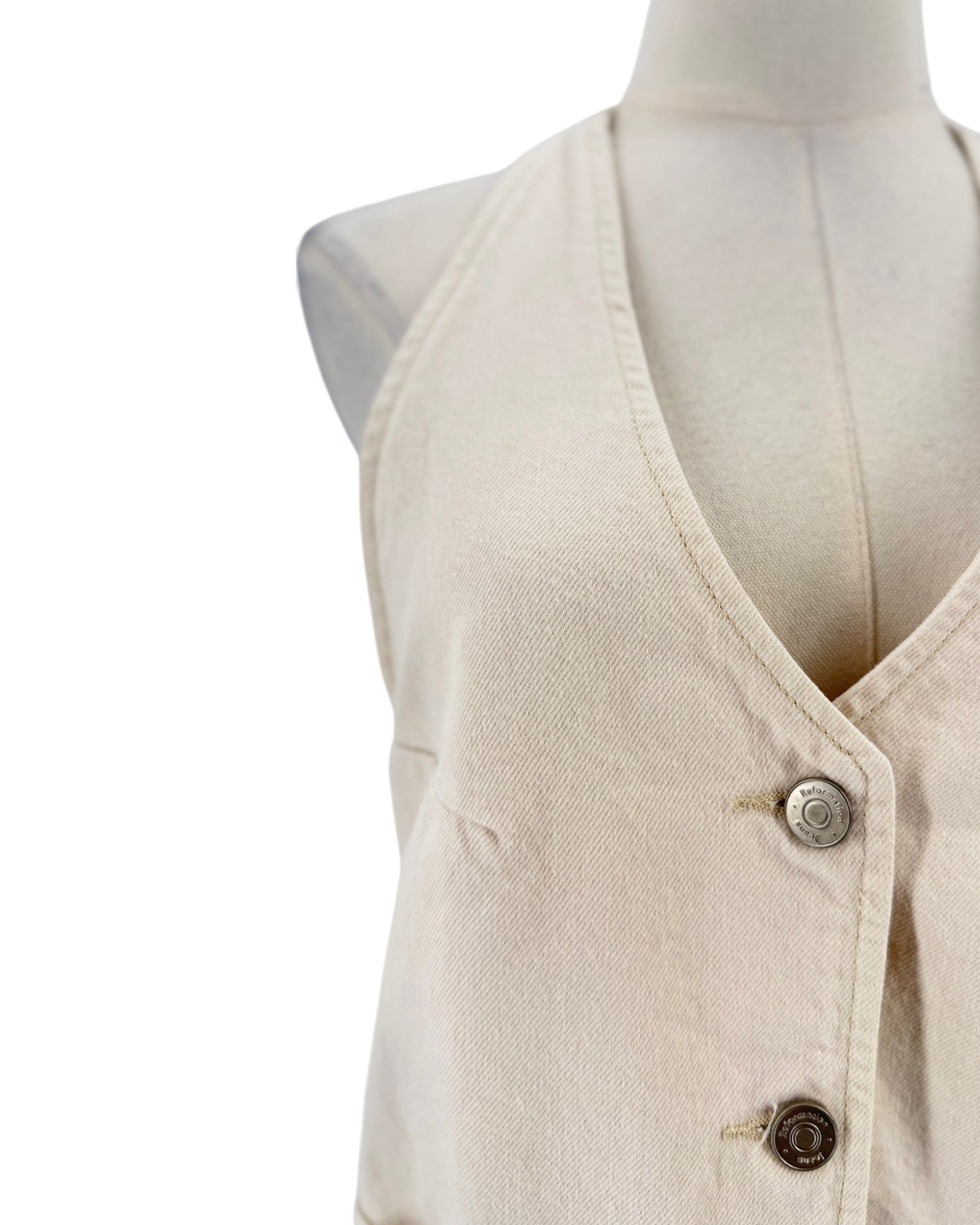 A close-up of a sleeveless cream-colored vest or tunic displayed on a mannequin torso against a plain white background.