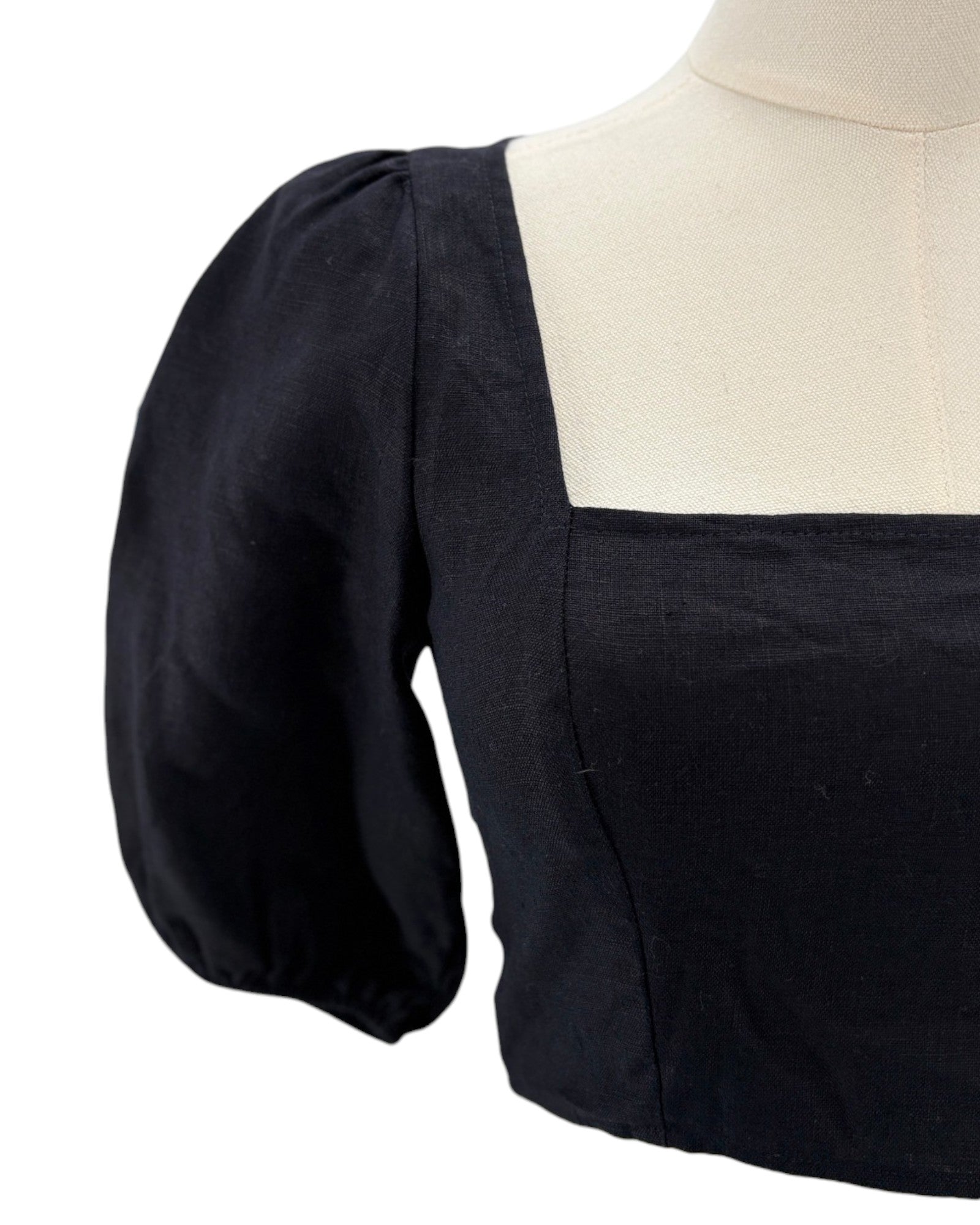 Reformation black blouse with puffed sleeves on a mannequin against a white background