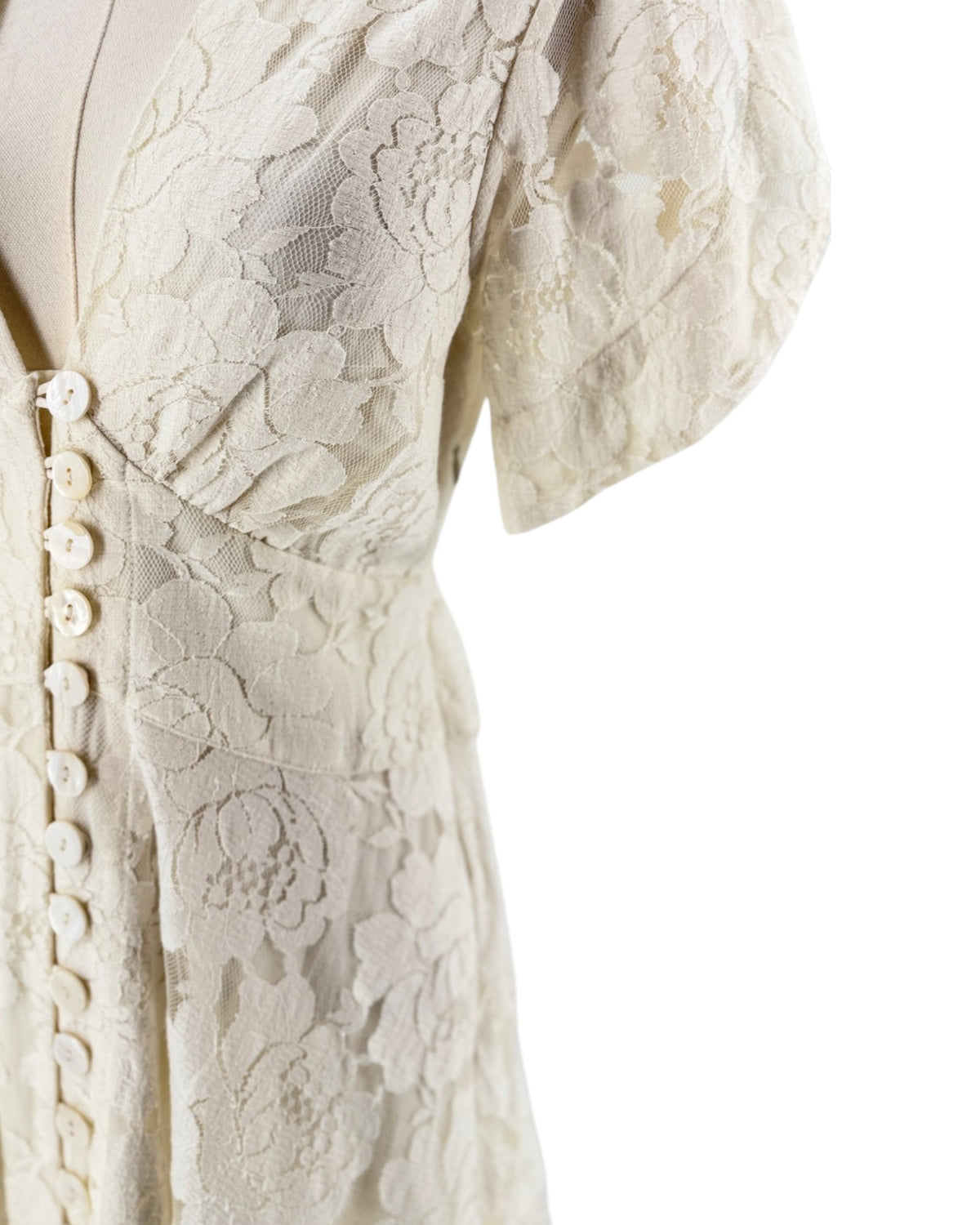 Close-up of a cream-colored lace dress on a mannequin, featuring short puff sleeves, a deep V-neckline, and a button-down front.
