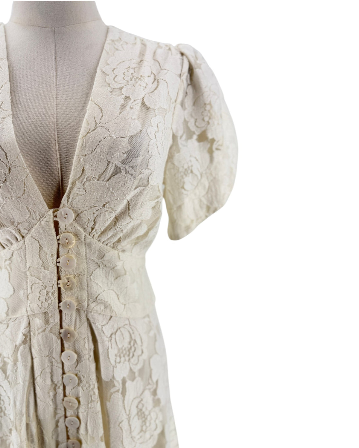 Close-up of a cream-colored lace dress on a mannequin, featuring short puff sleeves, a deep V-neckline, and a button-down front.