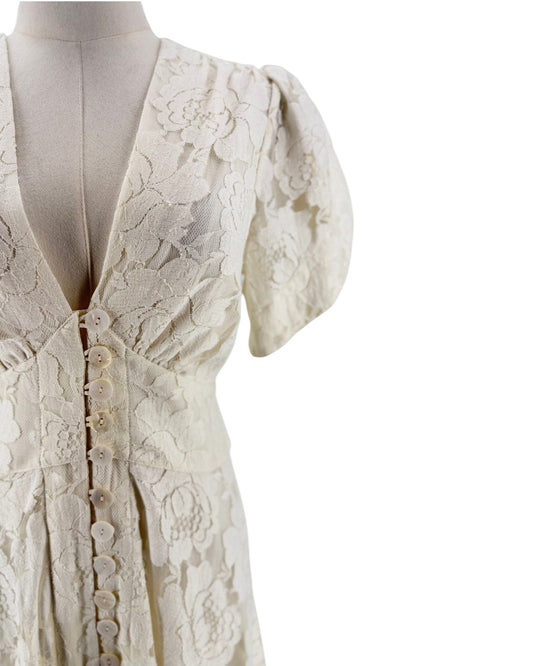 Close-up of a cream-colored lace dress on a mannequin, featuring short puff sleeves, a deep V-neckline, and a button-down front.