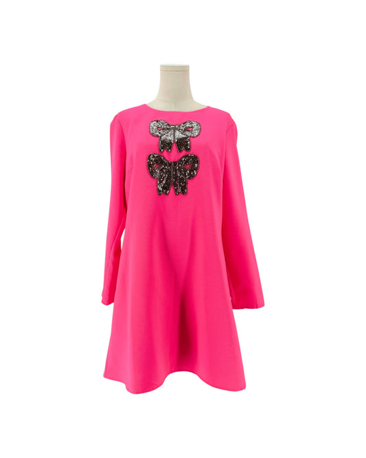 A bright pink long-sleeve dress displayed on a mannequin torso against a plain white background. The front features two sequined bow embellishments stacked vertically on the chest, one in silver and one in black.