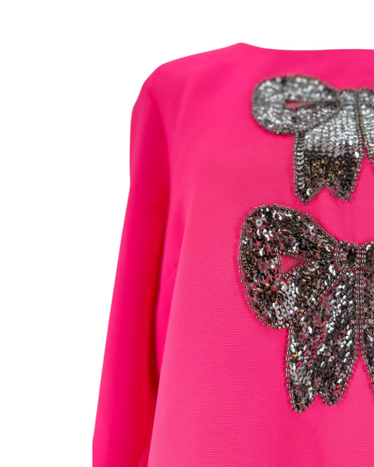 Bright pink long-sleeve top with large sequined bow embellishments on the chest, shown against a plain white background.