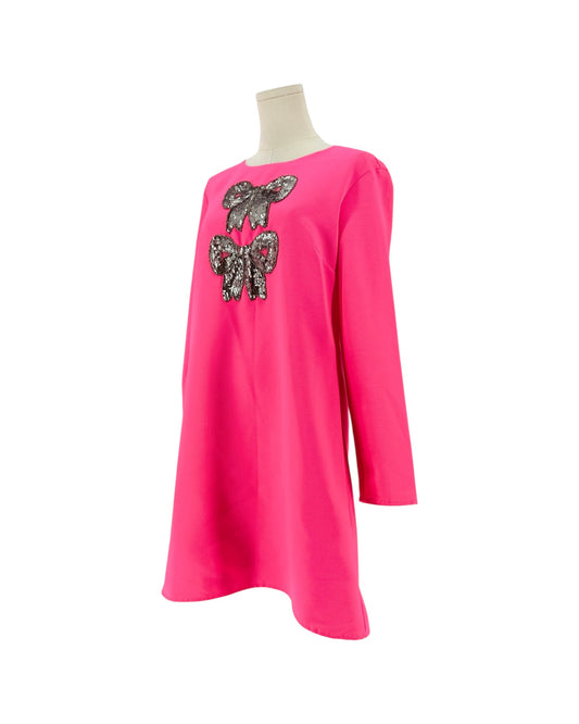 A bright pink long-sleeve tunic dress displayed on a mannequin torso against a plain white background. The front features a large sequined bow design in black, silver, and pink.