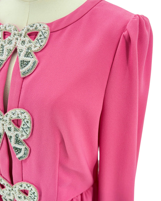 Close-up of a pink garment with decorative bow details on a white background