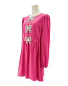 Pink dress with bow embellishments on a mannequin against a white background