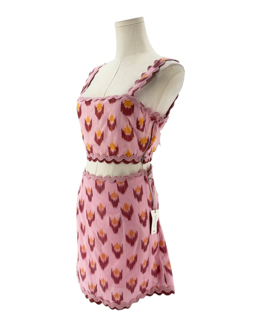 A pink two-piece set consisting of a sleeveless crop top and matching mini skirt, both featuring a repeating ikat-style pattern in dark red and yellow. The set is displayed on a cream mannequin torso against a plain white background.
