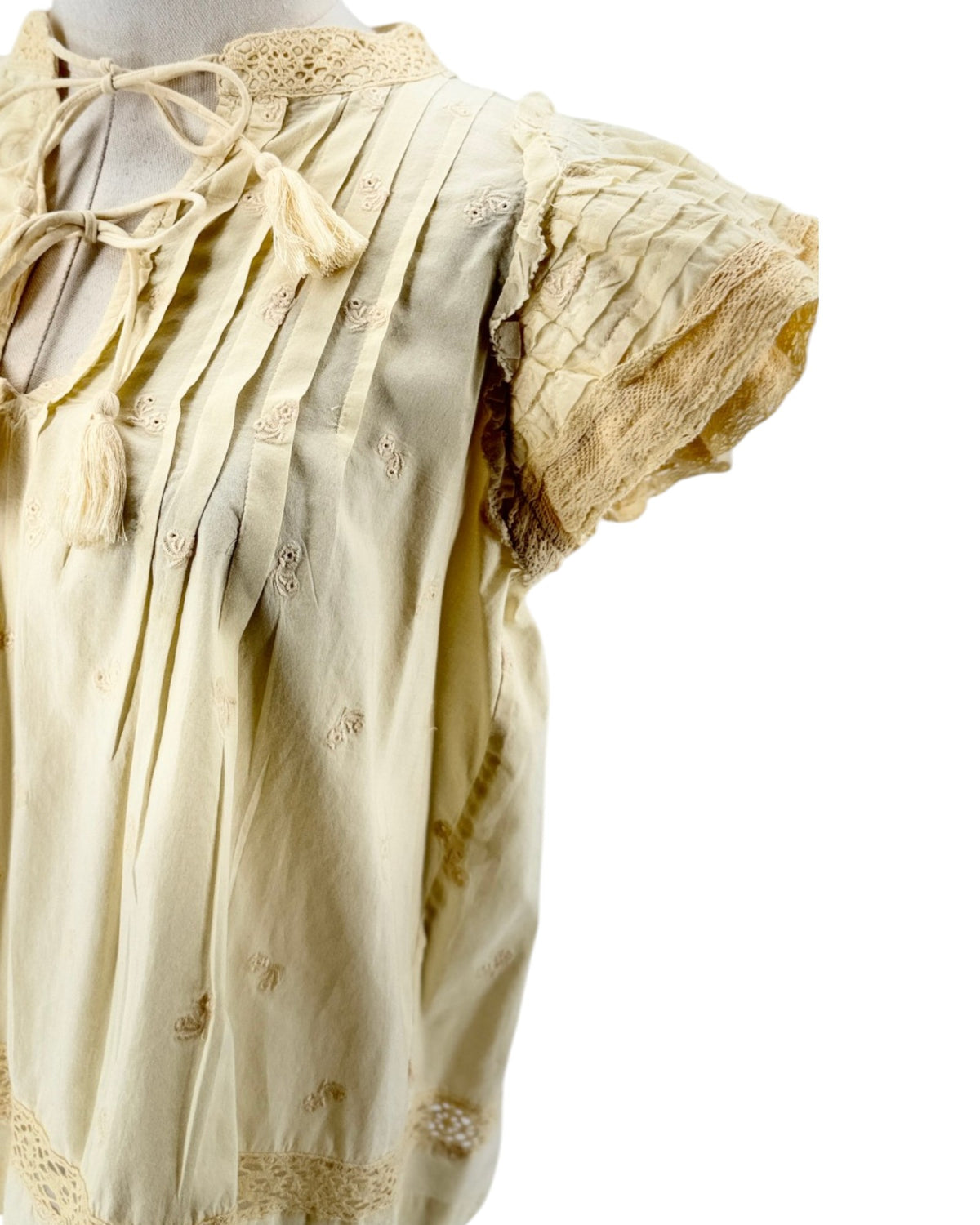 Cream short flutter sleeve blouse with tassel and embroidery details on a mannequin on a white background