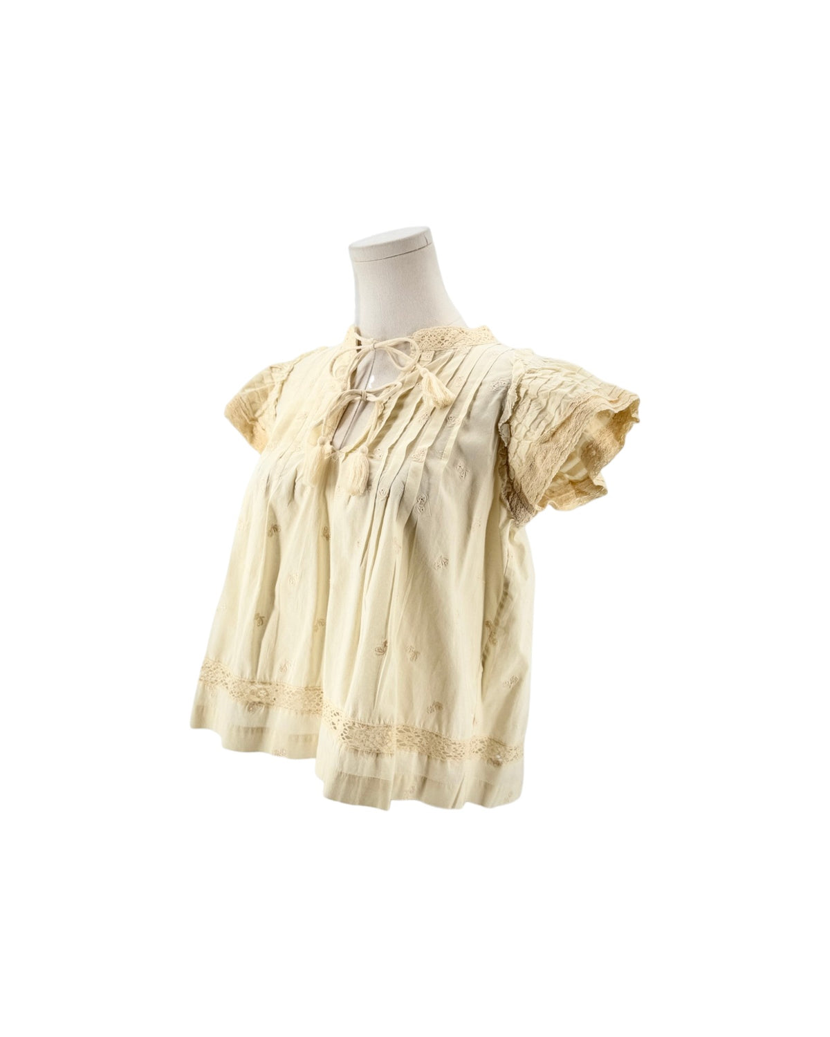 Cream short flutter sleeve blouse with tassel and embroidery details on a mannequin on a white background