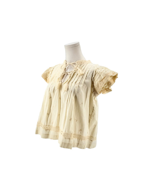 Cream short flutter sleeve blouse with tassel and embroidery details on a mannequin on a white background