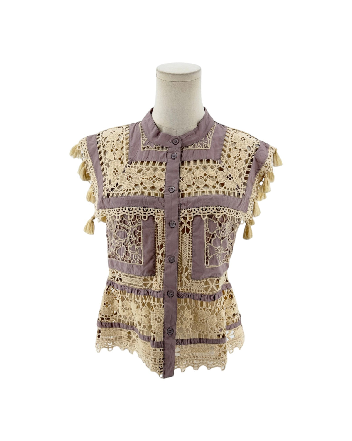 A sleeveless bohemian-style blouse with intricate crochet lace panels, tassel trim, and a button front, displayed on a mannequin torso against a white background.