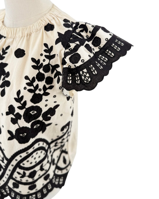 Cream with black applique throughout, flutter sleeves, scalloped hemline, elastic neckline on a white background on a mannequin