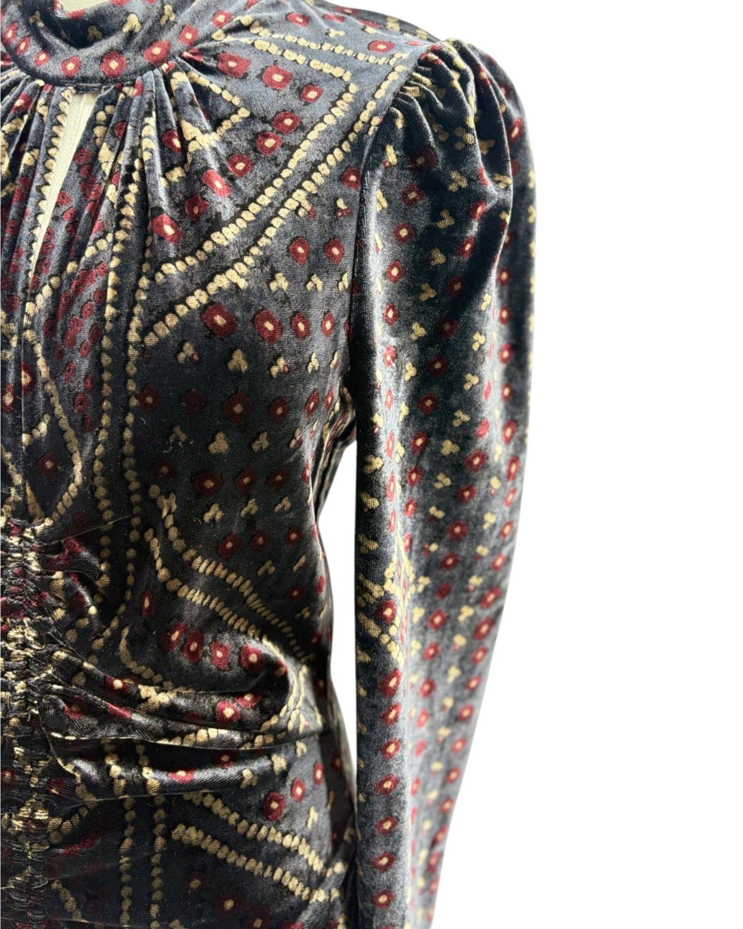 Close-up of a long-sleeve velvet top with a gathered high neckline and an intricate paisley-style pattern in beige, red, and gold on a dark gray background.