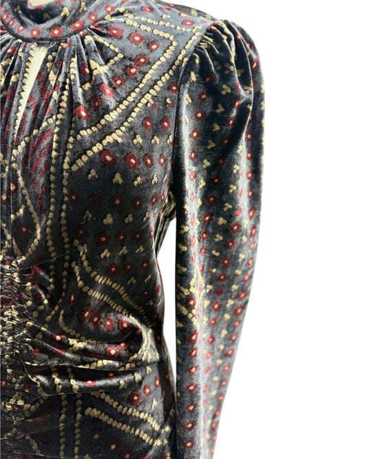 Close-up of a long-sleeve velvet top with a gathered high neckline and an intricate paisley-style pattern in beige, red, and gold on a dark gray background.