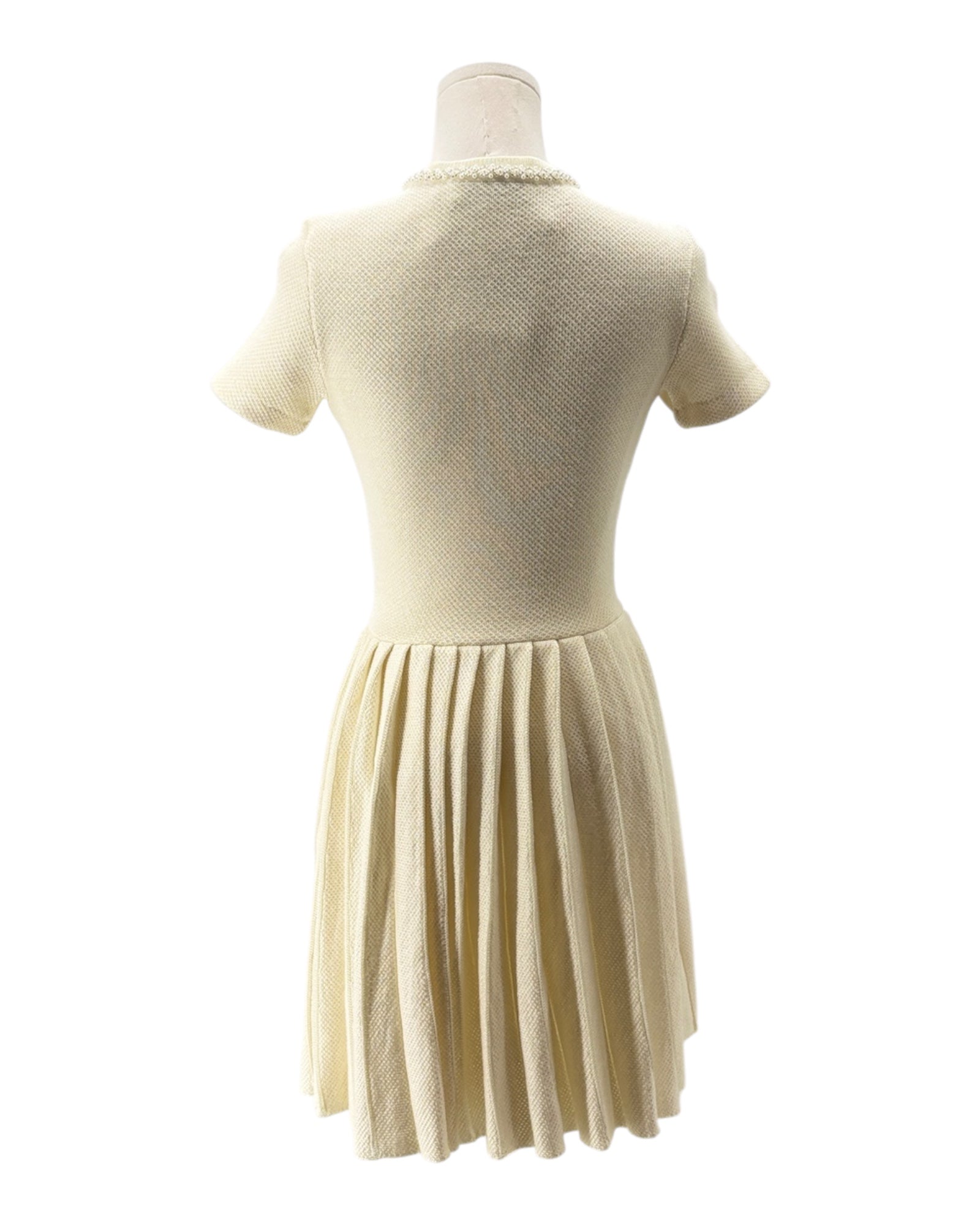 Mannequin wearing a cream-colored dress with a pleated skirt on a white background